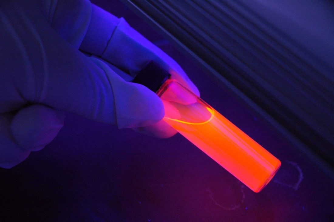 Close-up laboratory sample vial under blue and magenta lighting
